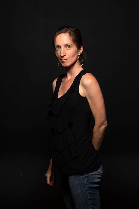 Author's headshot of Kari Kwinn, wearing a black tank top and wire earrings in front of a black background